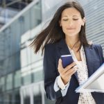 üzletasszony irodaépületek között halad mobilon ügyeket intéz