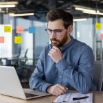 komoly arcú vállalkozó laptopot néz íróasztalnál
