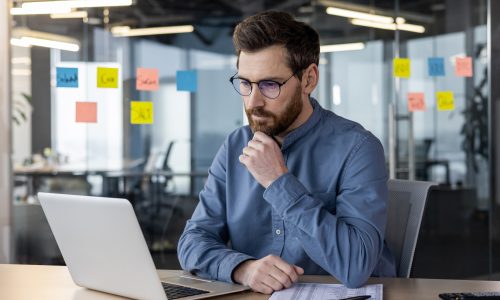 komoly arcú vállalkozó laptopot néz íróasztalnál
