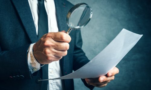 öltönyös férfi nagyítóval vizsgál egy dokumentumot