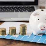 laptop, kimutatások, malacpersely mellette érmék toronyba rendezve